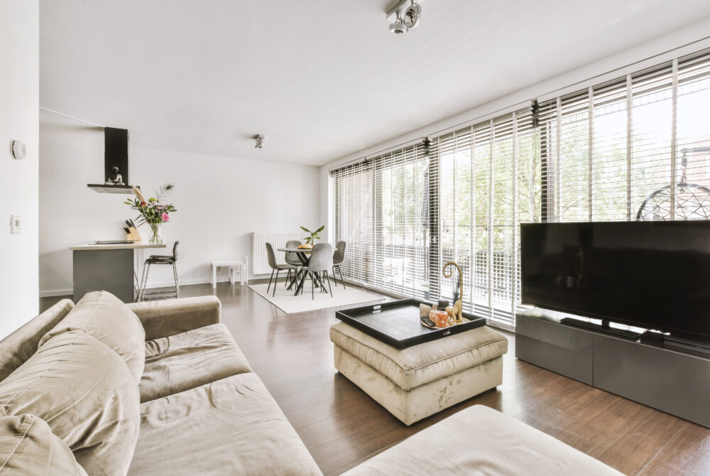 Contemporary minimalist style interior design of light studio apartment with wooden table and chairs in dining zone between open kitchen and living room with white walls and parquet floor
