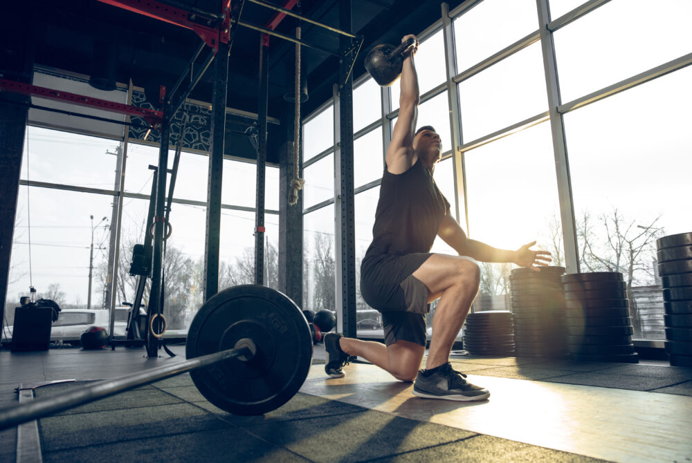 Control. Young muscular caucasian athlete training in gym, doing strength exercises, practicing, work on his upper body with weights and ball. Fitness, wellness, sport, healthy lifestyle concept.